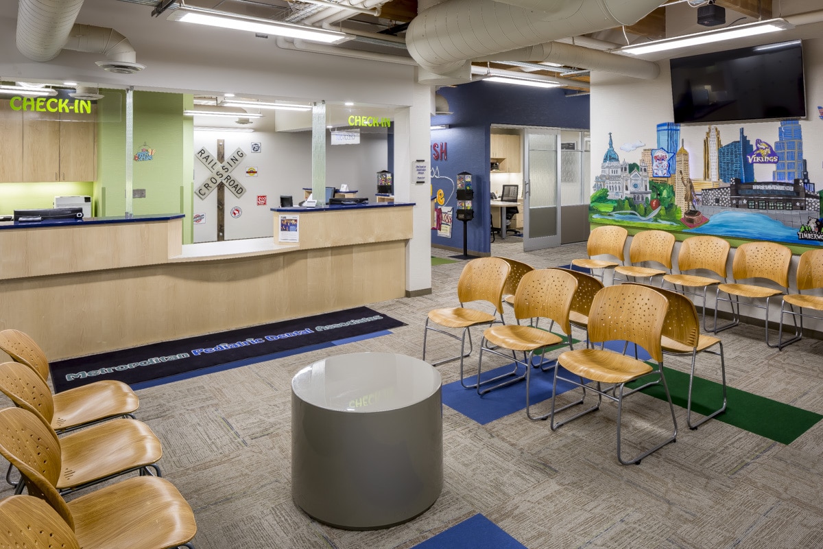 A waiting room with check-in desk, chairs, mural of Pittsburgh's skyline, and a person. Bright lighting and modern design elements are present.